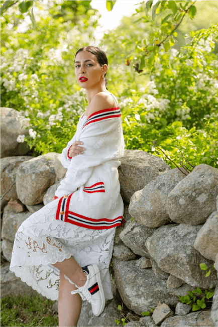 Alexa sitting on rocks outdoors, surrounded by green foliage, wearing a white sweater with red and navy stripes.